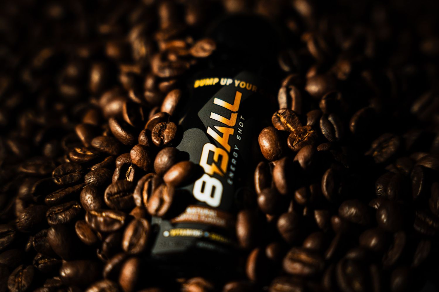 Black energy drink can lying among scattered dark roasted coffee beans in dramatic lighting.