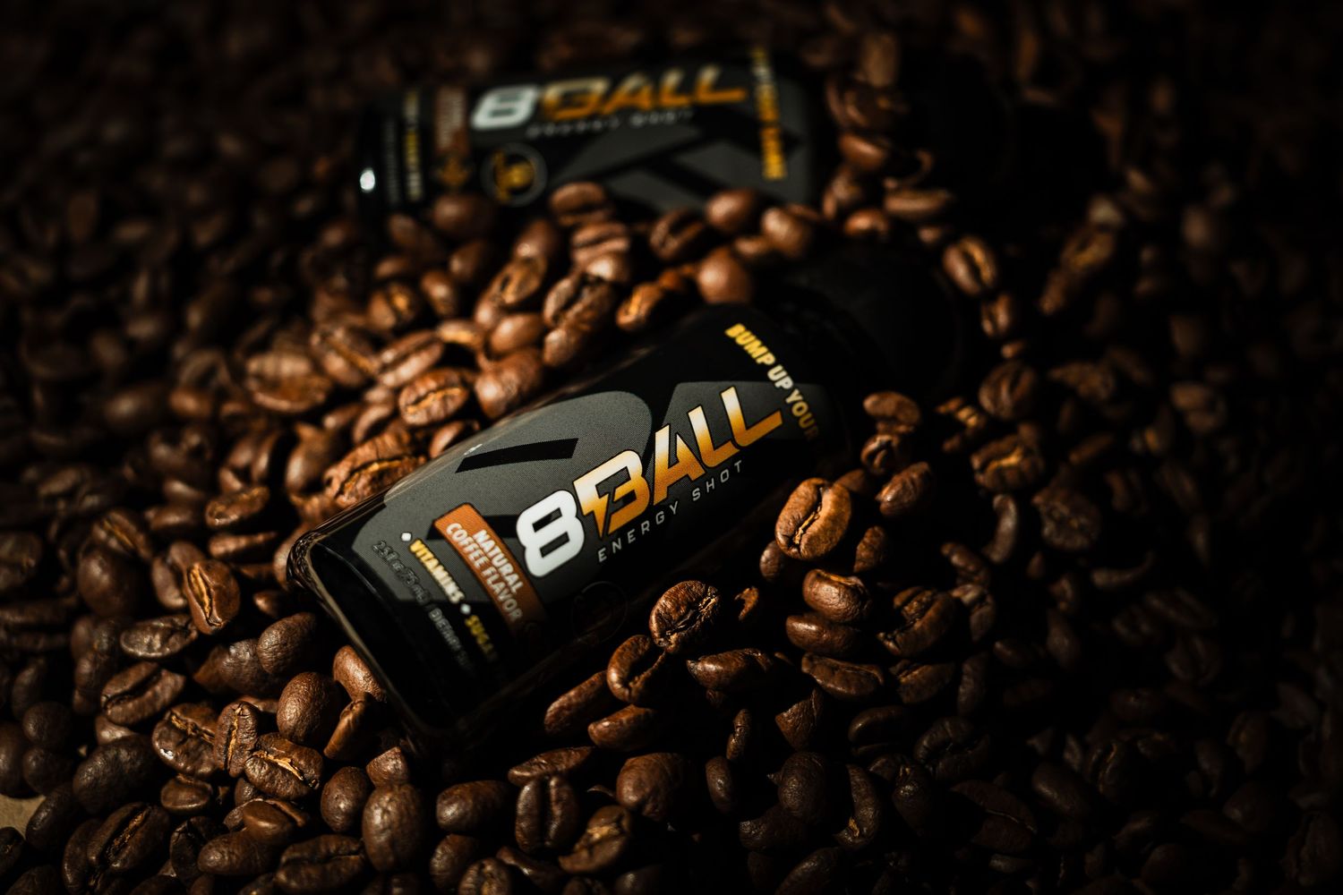 BBALL energy drink cans nestled in a bed of roasted coffee beans with dramatic lighting and shallow depth of field.