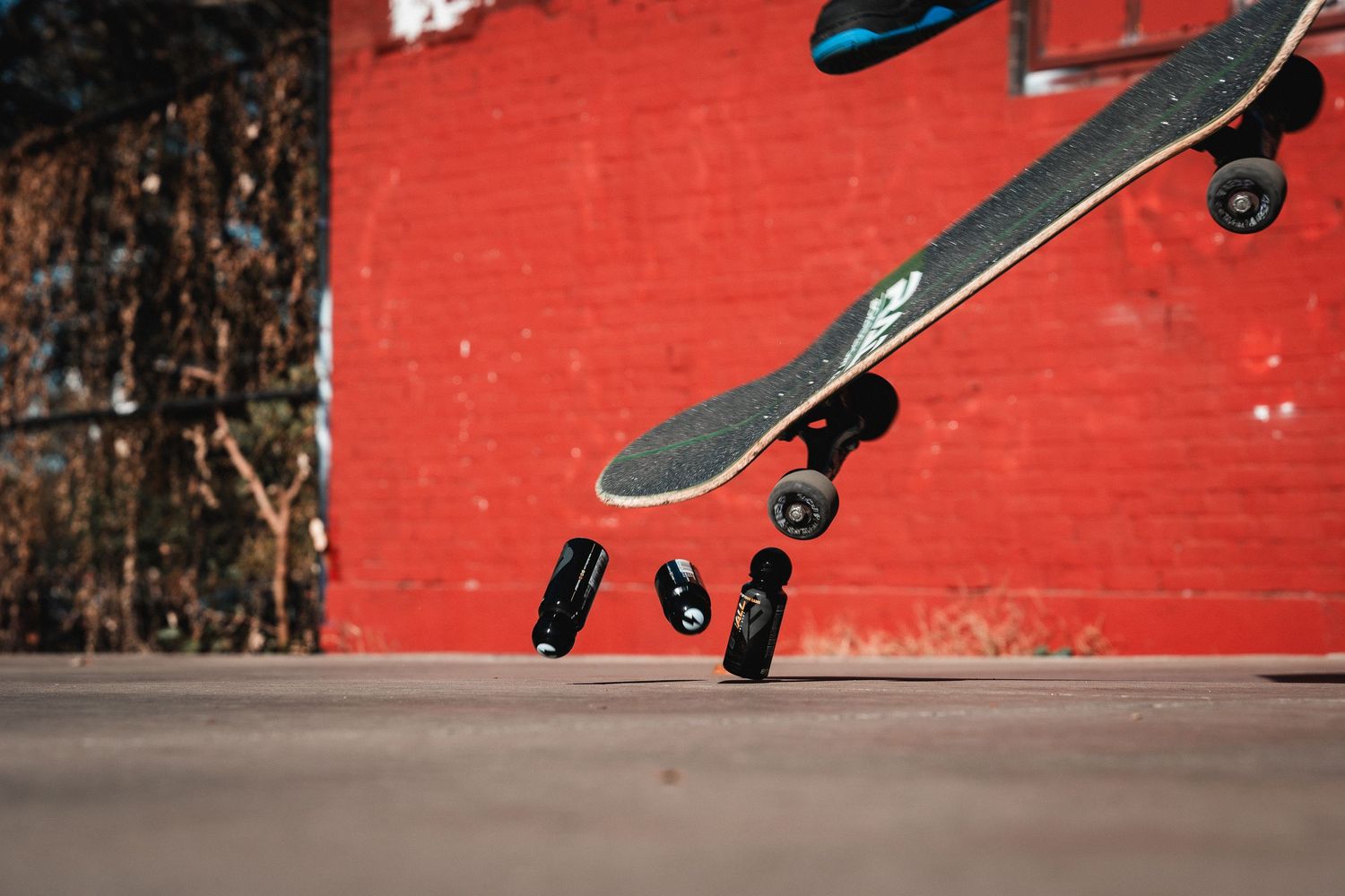 Close-up of a skateboard performing an ollie trick against a red wall backdrop.