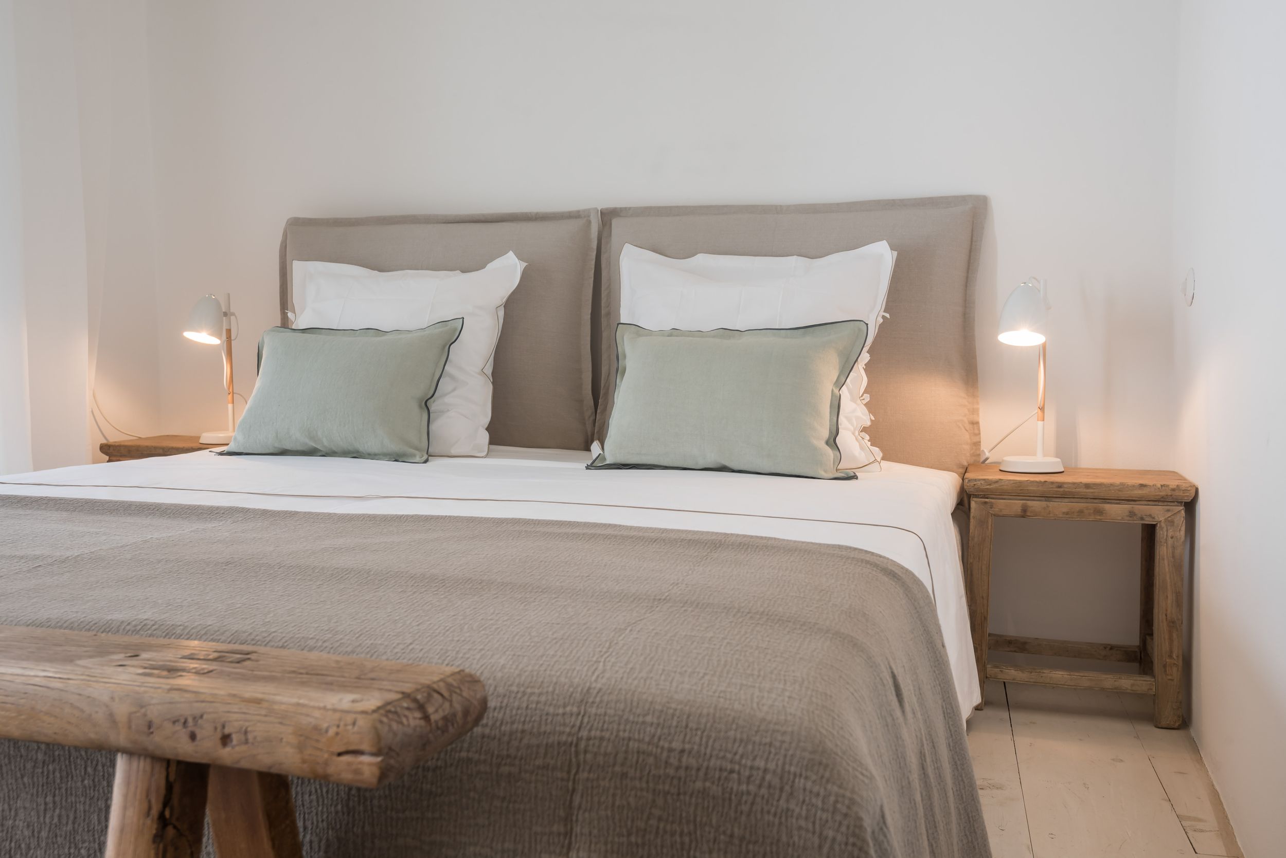 Neutral bedroom with twin bedside lamps, taupe headboard, and rustic wooden bench.