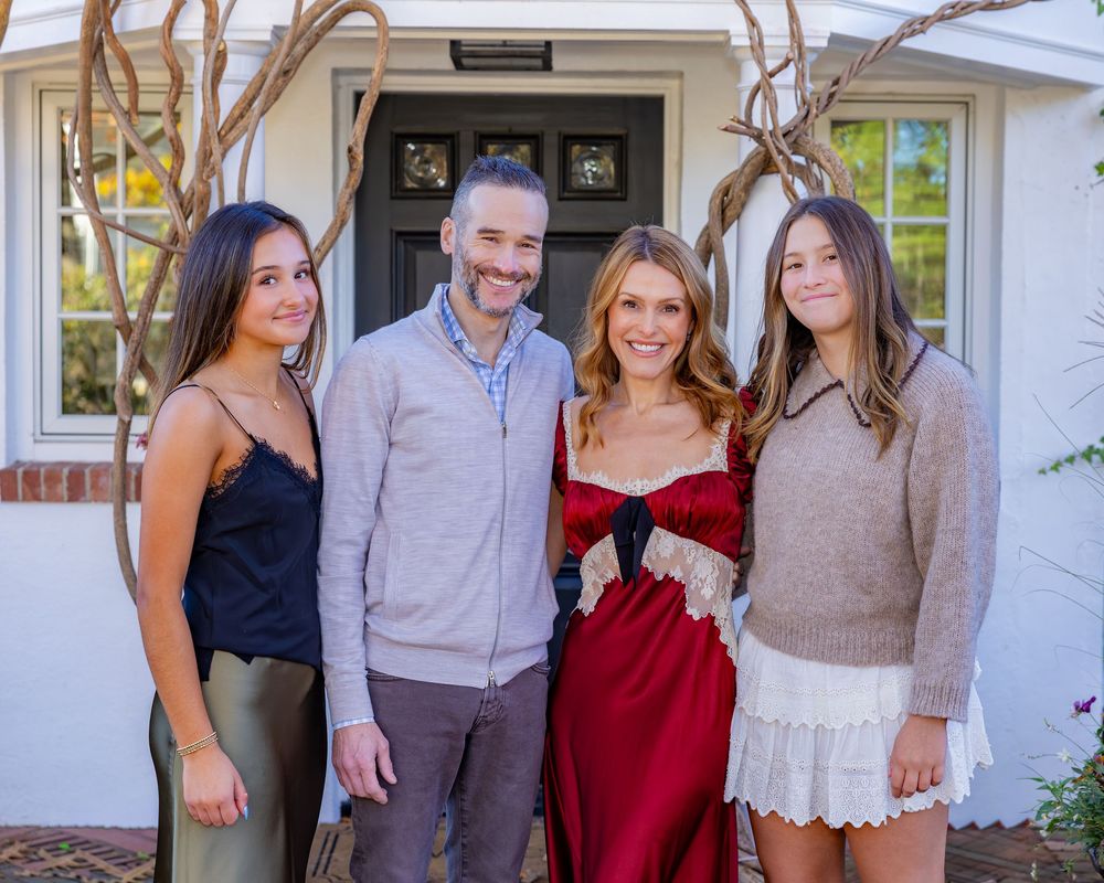 Family poses together smiling in front of their home entrance on a sunny day during a family photography session in Concord, MA.