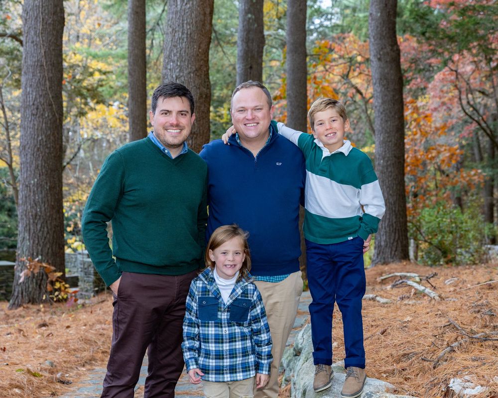 A family wearing casual clothing poses together outdoors among autumn trees on a stone path during a family photography session in Sudbury.