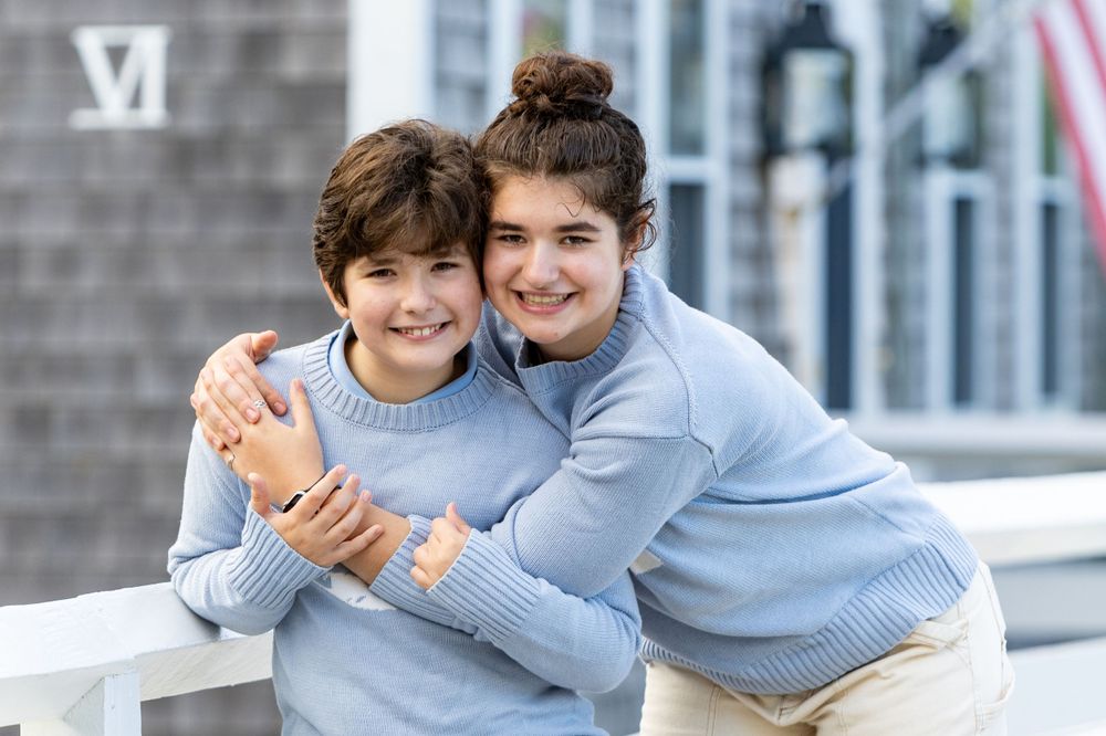 Siblings sharing a joyful moment together on a bridge in Sconset beach during a family photoshoot on Nantucket, Massachusetts.