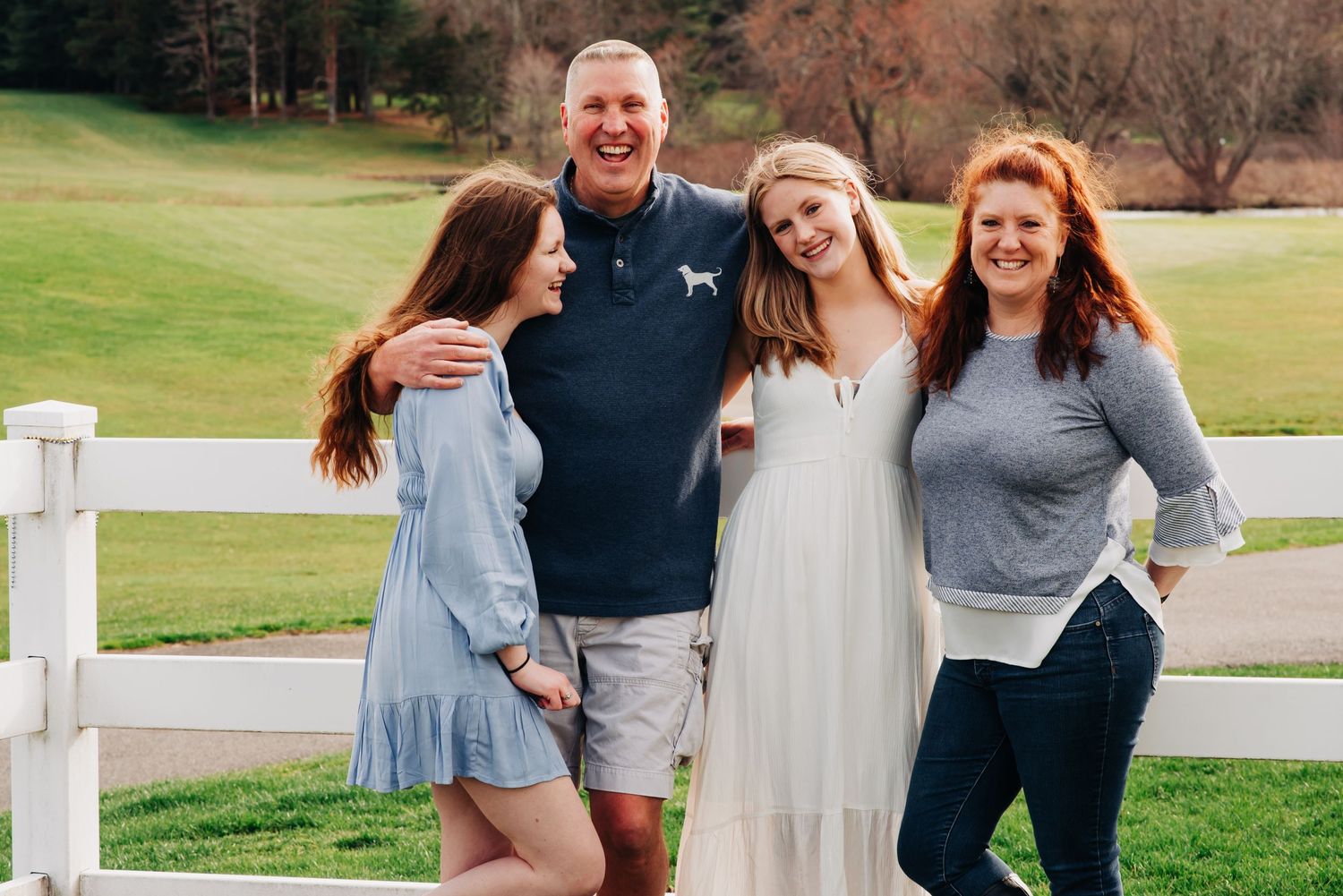 A beautiful family portrait of a family against a white fence  with grass behind them