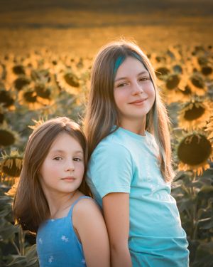 Two children sitting together in a sunflower field at golden hour with warm sunset lighting.
