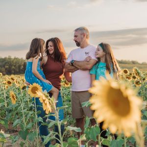 A family enjoys quality time together in a vibrant sunflower field during golden hour sunset.