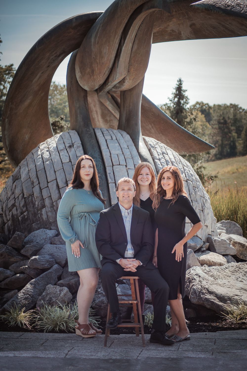 Group portrait in front of large abstract sculpture outdoors.