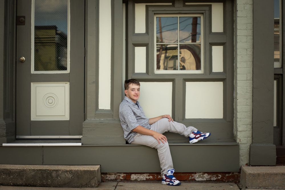 A youth sits casually on a grey building ledge wearing athletic shoes.
