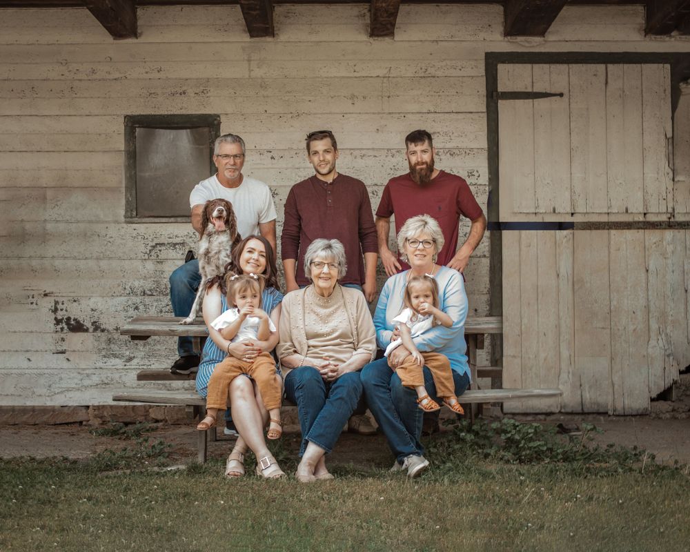 Multi-generational family gathering poses together outside rustic wooden building.