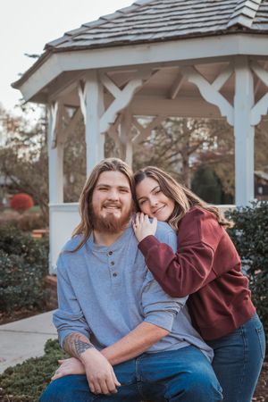 A couple shares a tender moment together while sitting under a white gazebo on a sunny day.