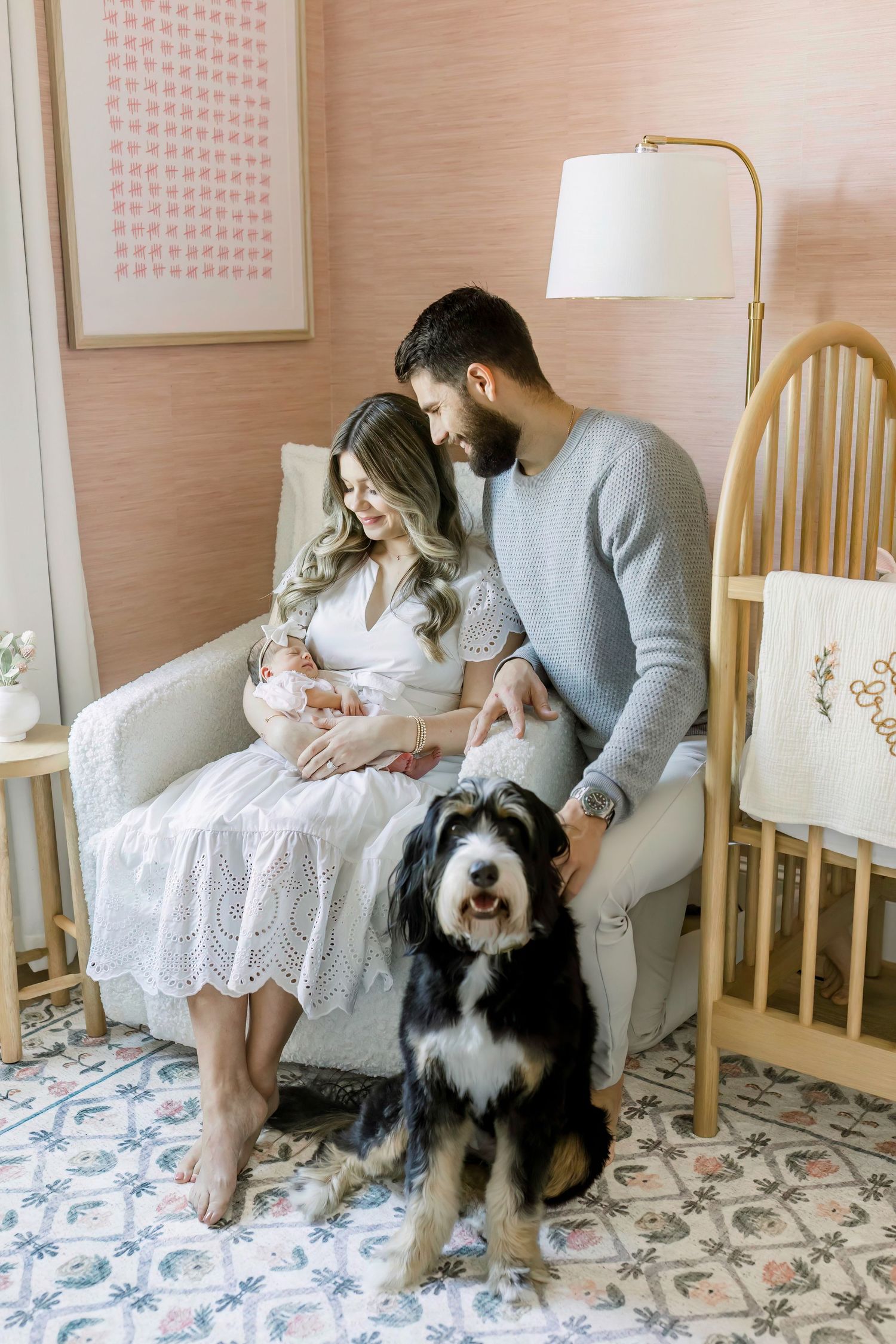 Family portrait in nursery with black and white dog sitting beside armchair.