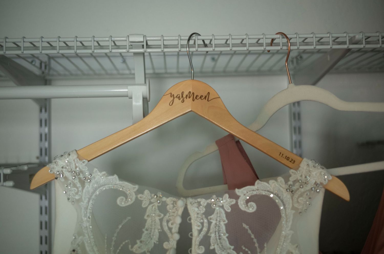 A wooden bridal hanger displayed on a closet rack with delicate lace details.