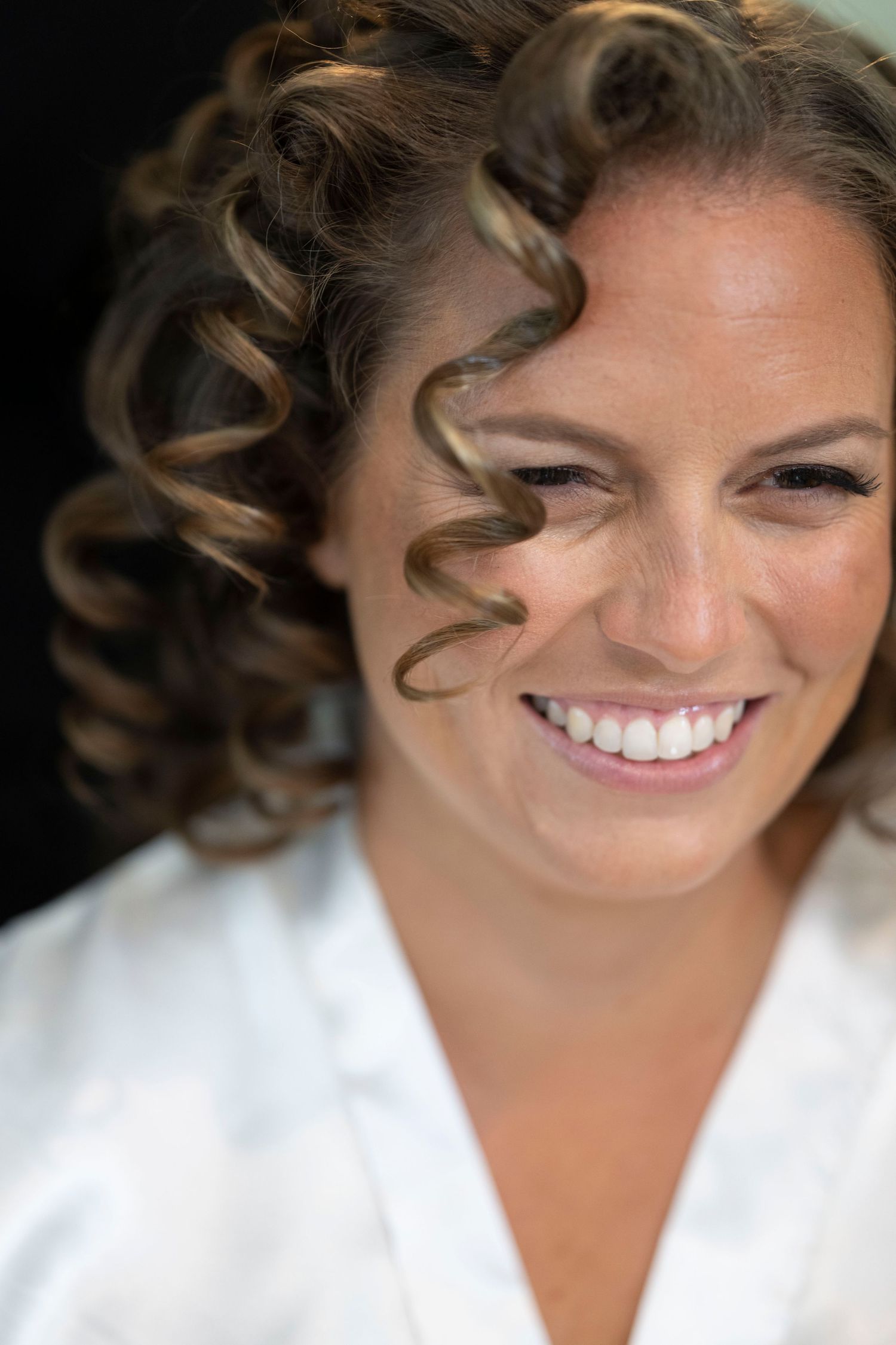 A close-up portrait showing elegant curled hairstyling and natural wedding makeup.