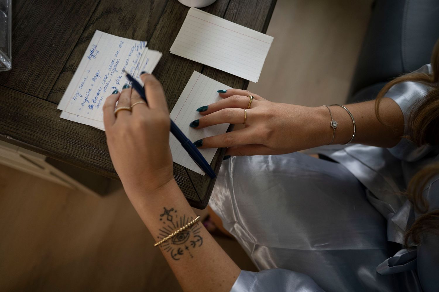 Hands with delicate tattoos and jewelry writing on wedding preparation documents.