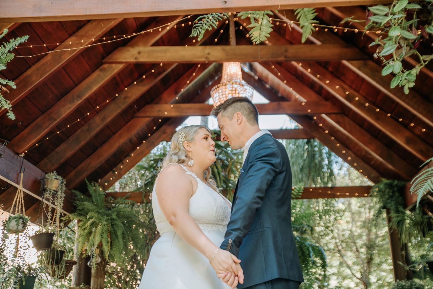 A romantic moment between newlyweds under a wooden gazebo decorated with greenery.