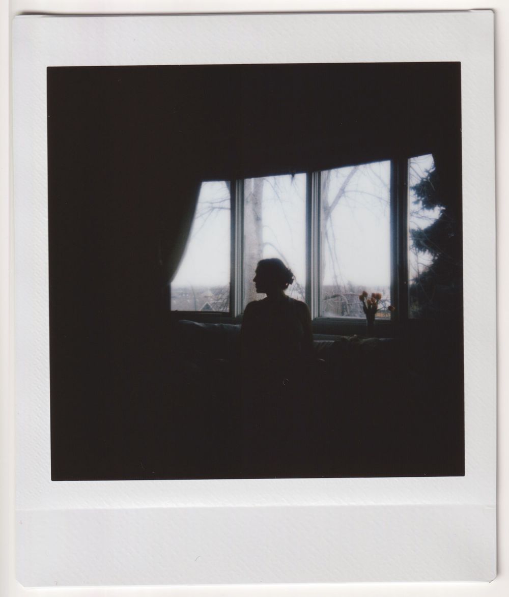 Silhouette against windows creating dramatic contrast in black and white Polaroid photo.