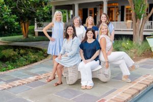 Group of friends sitting together on stone bench in front of coastal home on summer day.