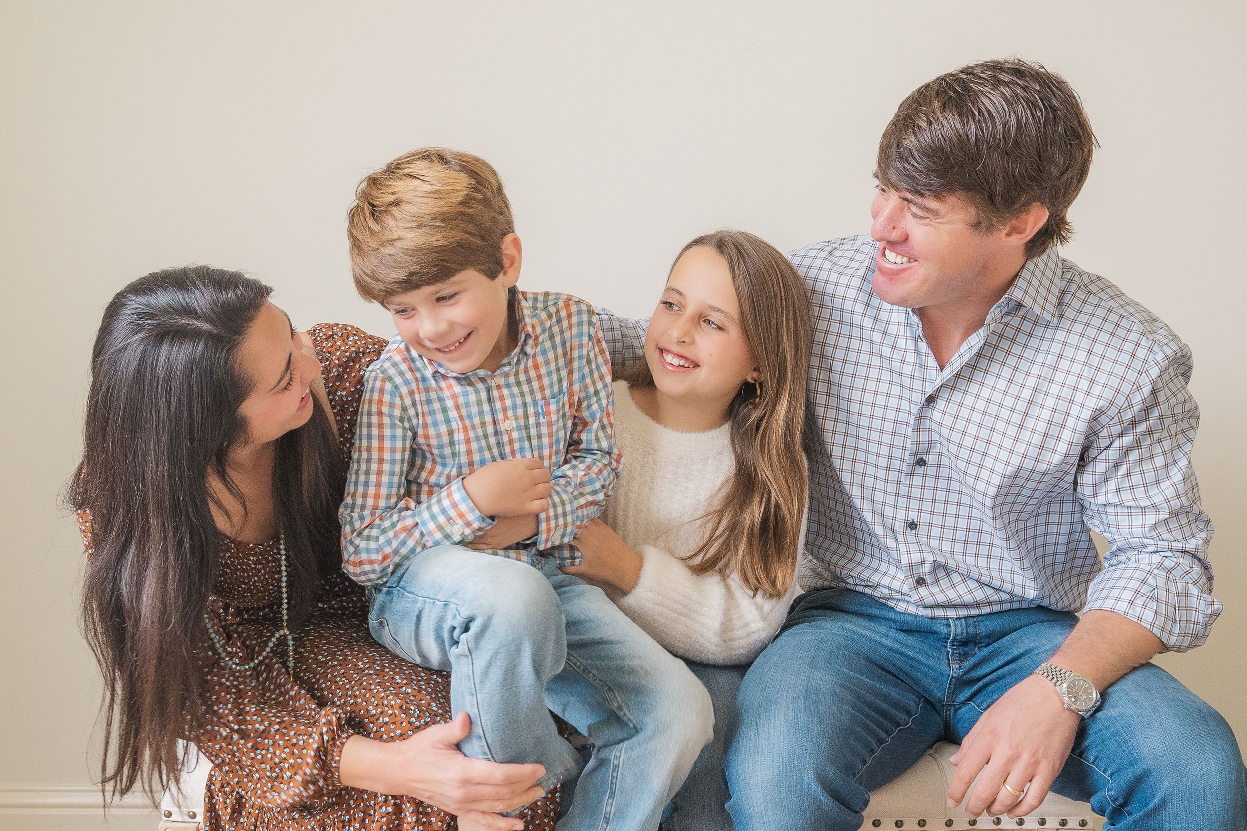 Family of four sitting close together on couch sharing intimate moment in casual attire.