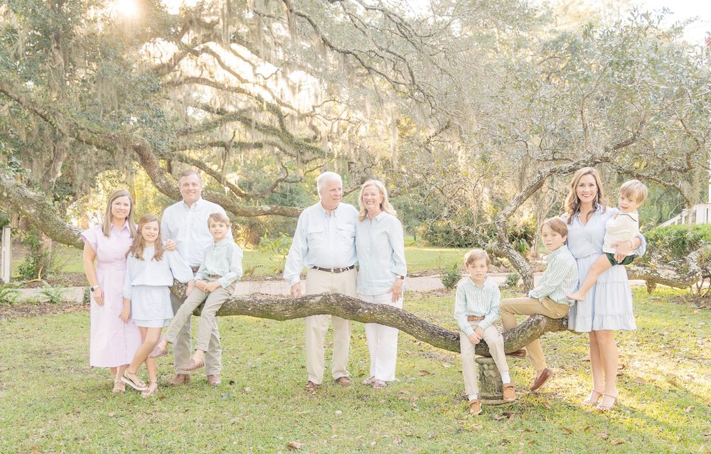Extended family portrait in white and blue clothing at sunset under oak trees.