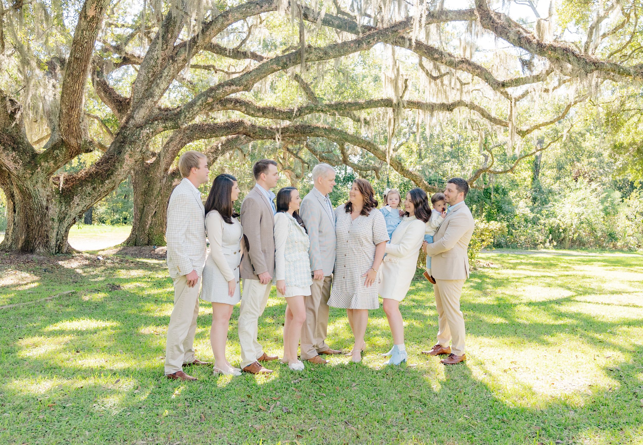 Group wearing coordinated light colored outfits posing under Spanish moss draped tree.