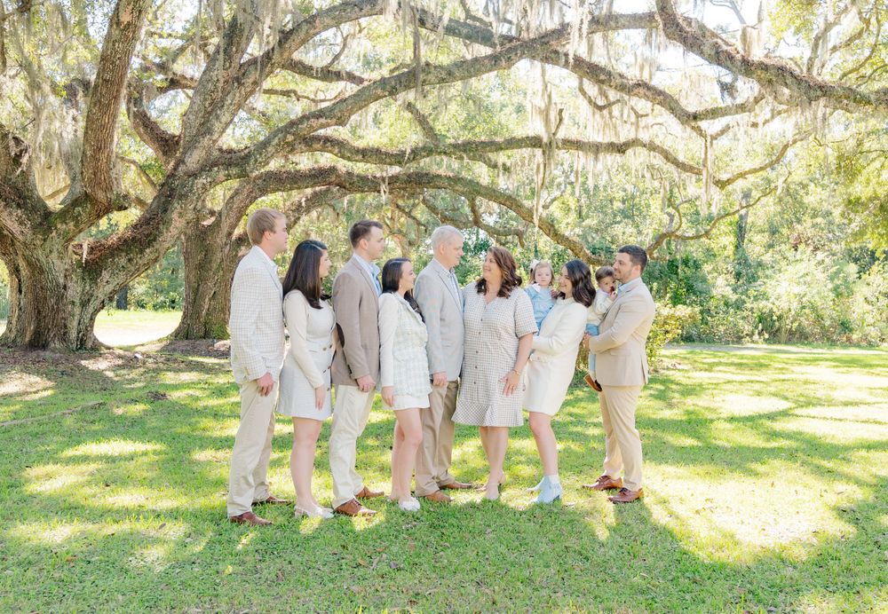 Group wearing coordinated light colored outfits posing under Spanish moss draped tree.