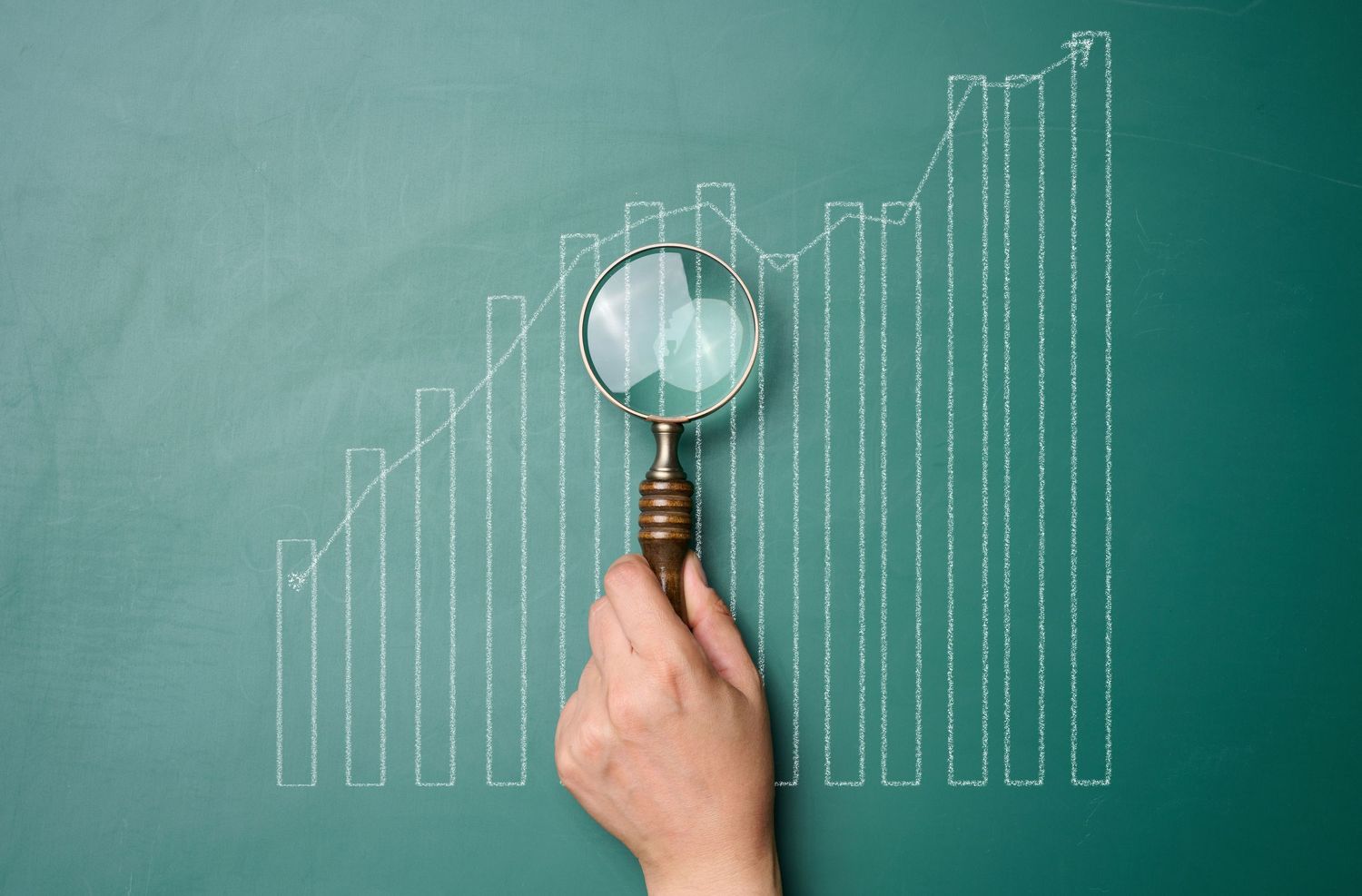 A graph drawn with white chalk with growing indicators and a woman's hand with a magnifying glass. Business indicators g