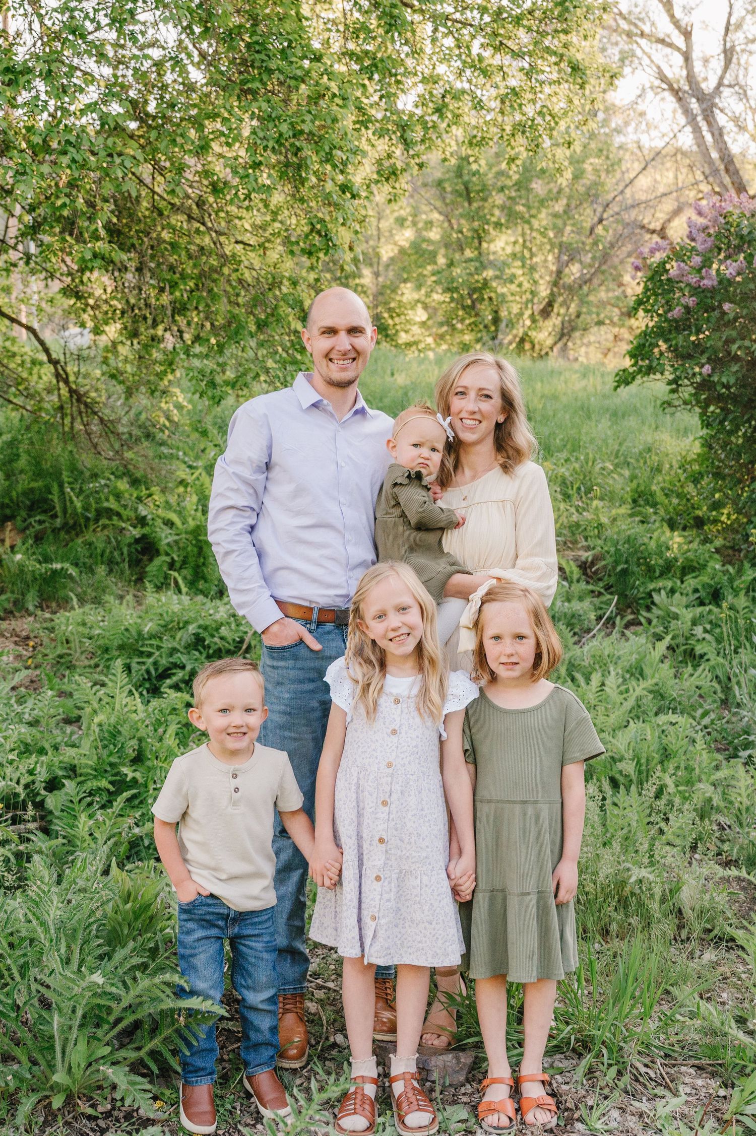 Family group photo outdoors in natural setting with green foliage and trees in background.