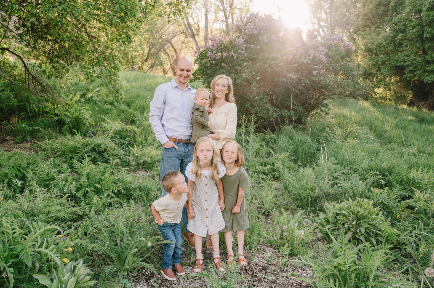 A group standing together on a sunlit forest path surrounded by lush green ferns and vegetation during golden hour.