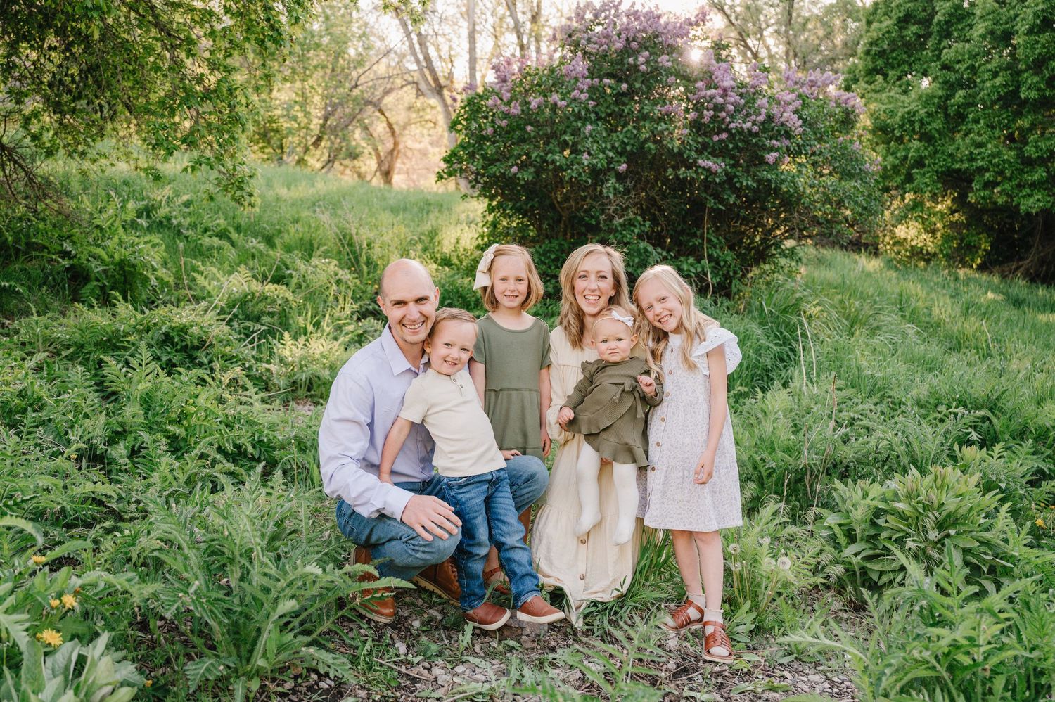 A family gathers together outdoors on a spring evening surrounded by lush green foliage and blooming plants.