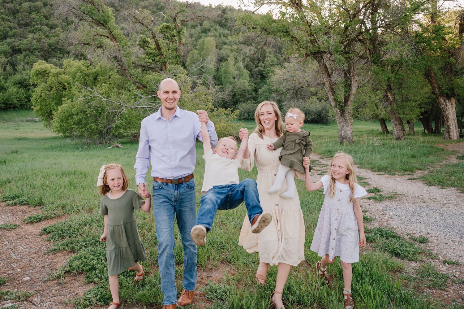 A group enjoys a playful moment together while walking along a dirt path surrounded by lush green trees and grass.