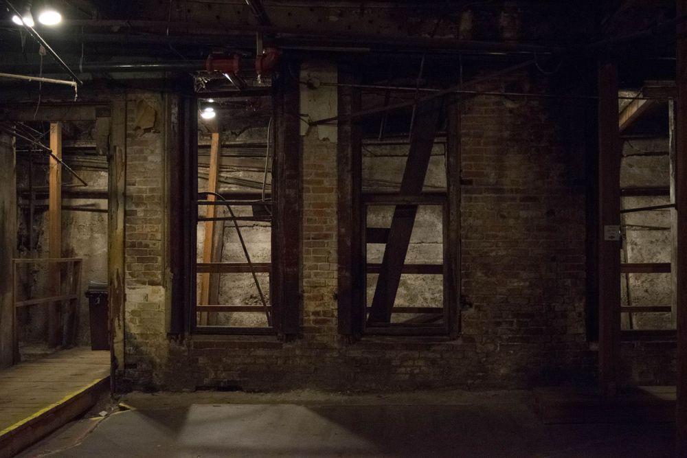 Dark industrial basement with exposed brick walls and windows casting shadows.