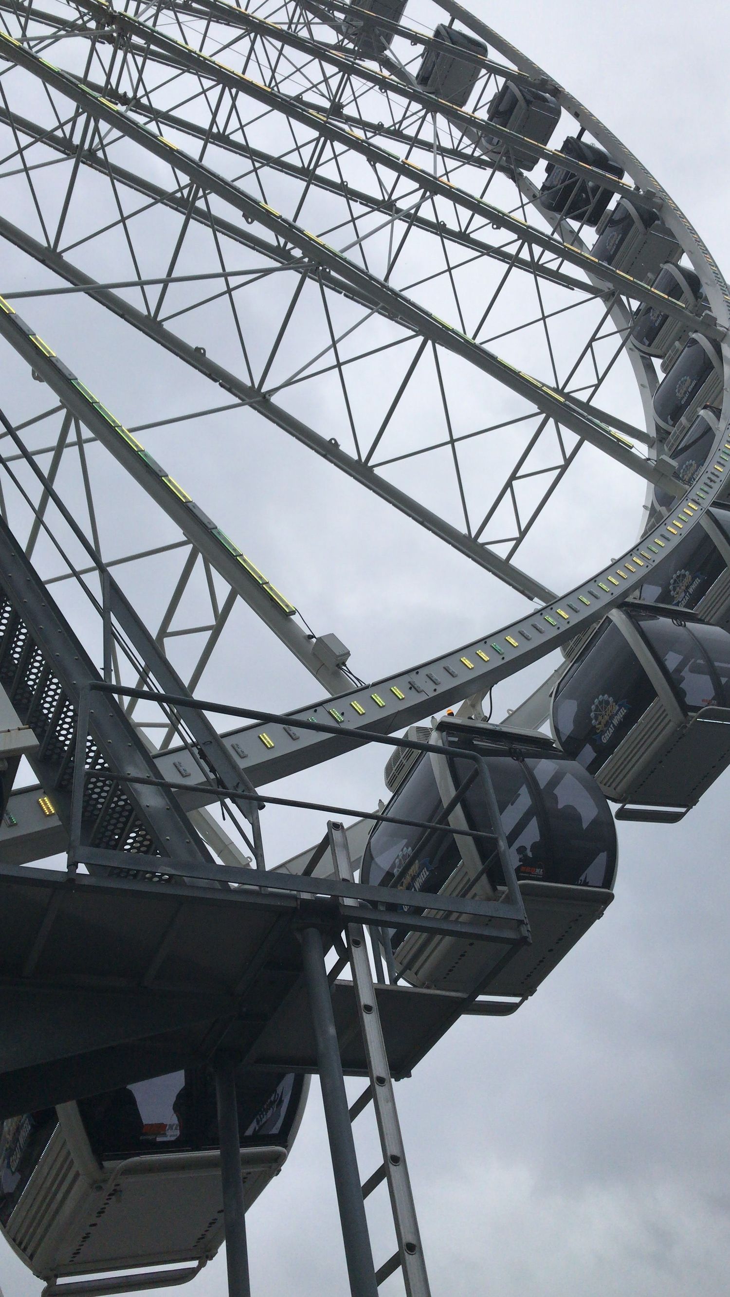 Close-up view of a Ferris wheel's metal support structure and gondolas against an overcast sky.