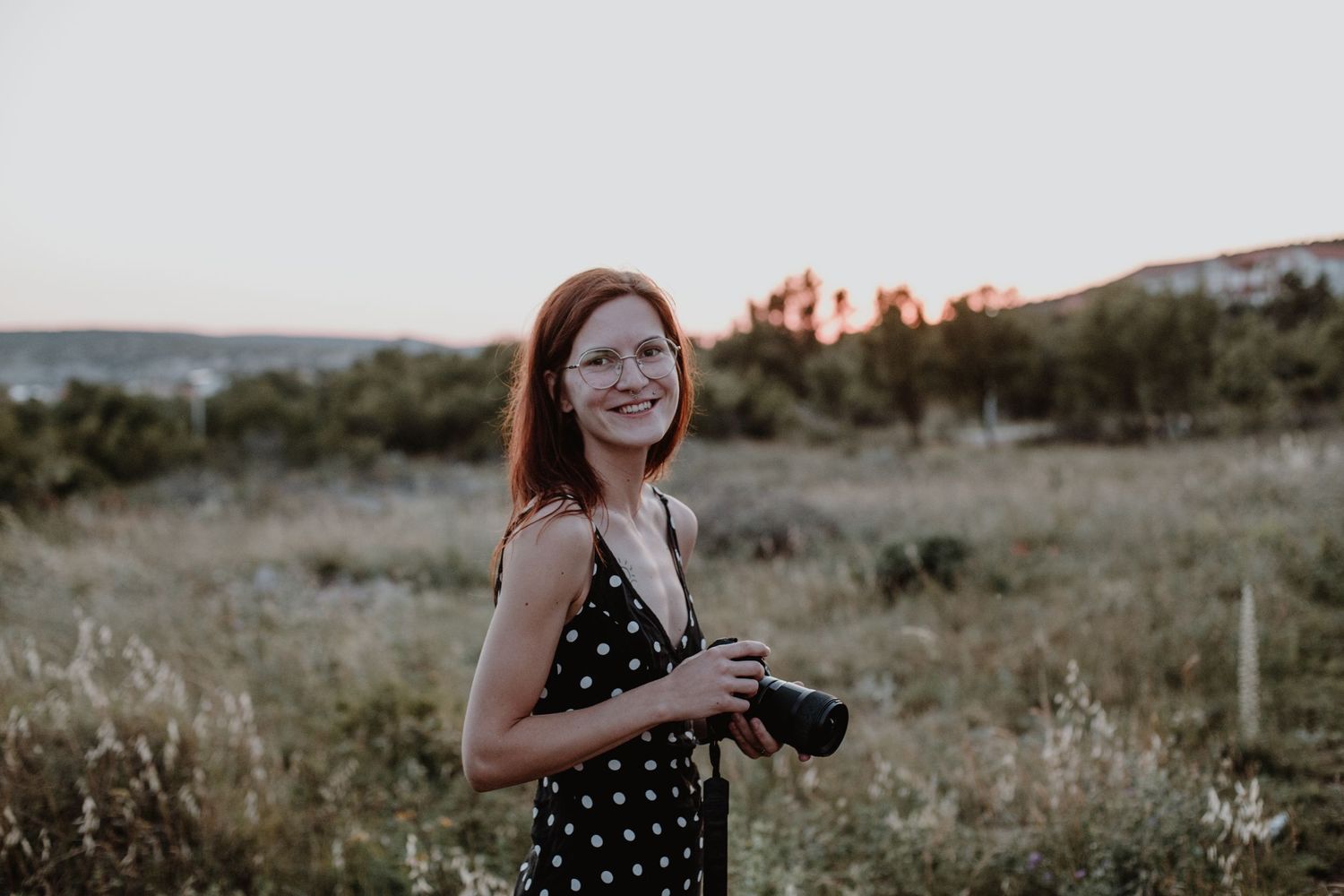 Person with camera enjoying sunset in natural outdoor setting with tall grass.