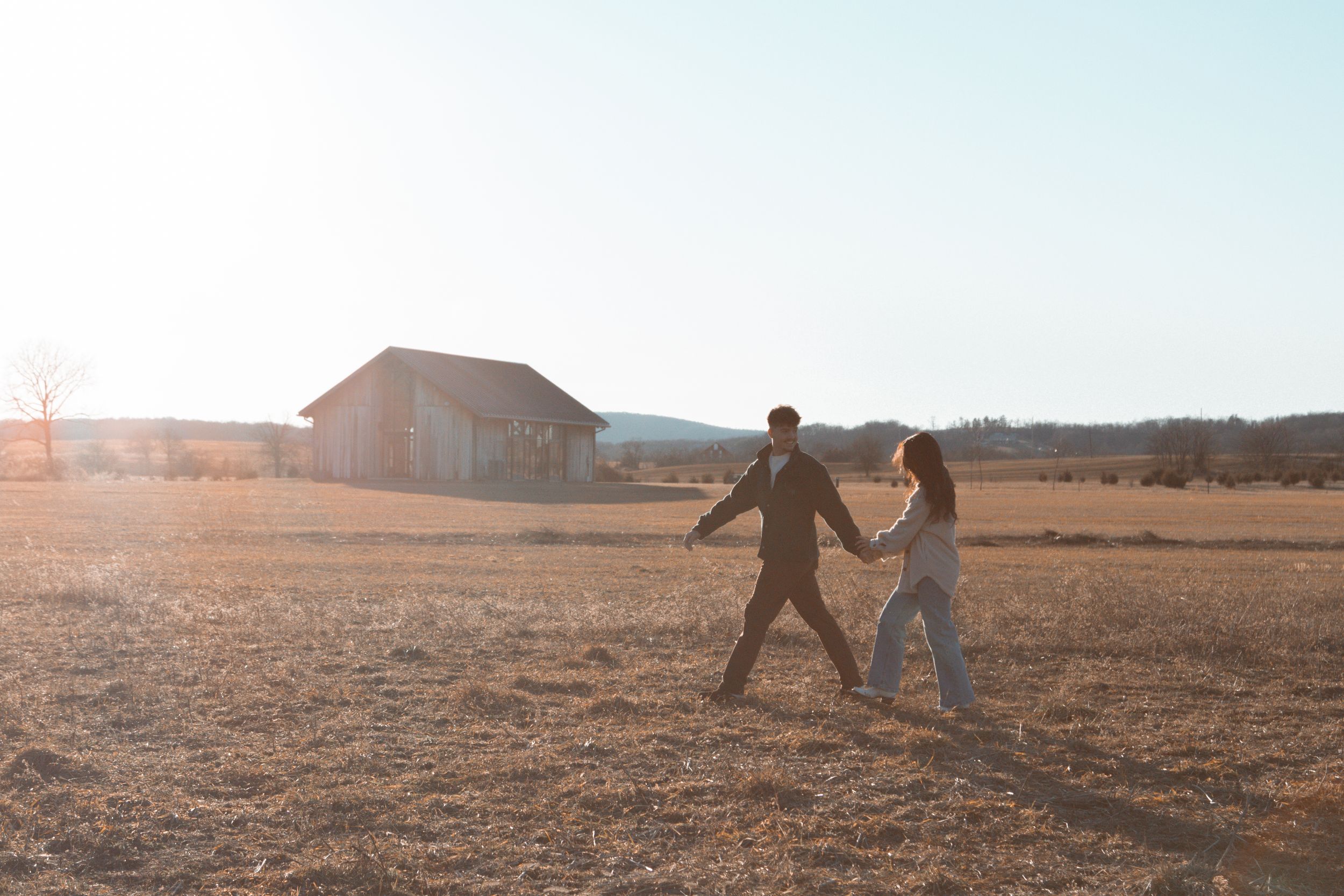 Playful couple running through field at sunset during wedding photoshoot.