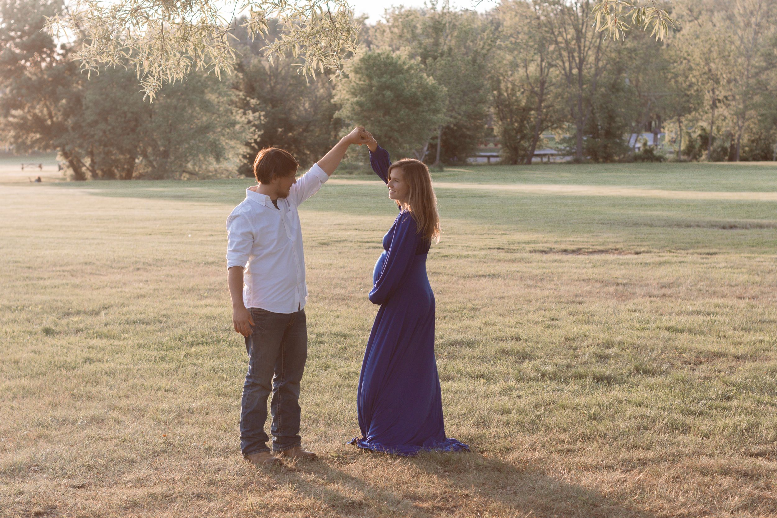 A couple shares intimate moments during their outdoor maternity photoshoot at sunset.