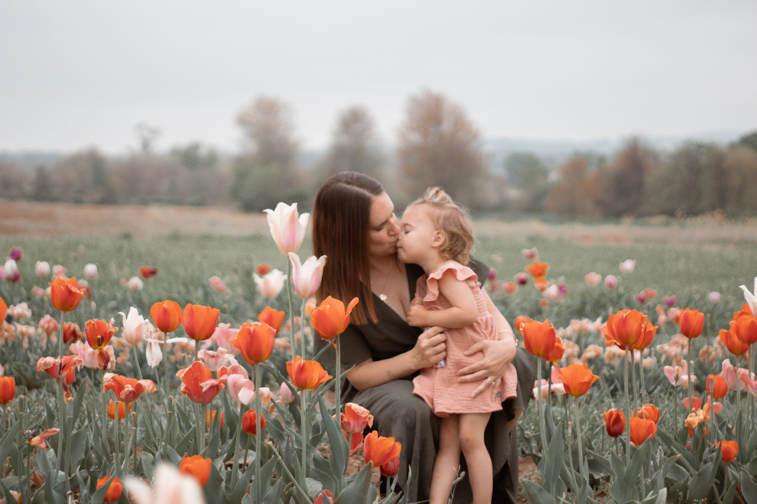 A tender moment shared in a vibrant tulip field with orange and pink blooms on a cloudy spring day.