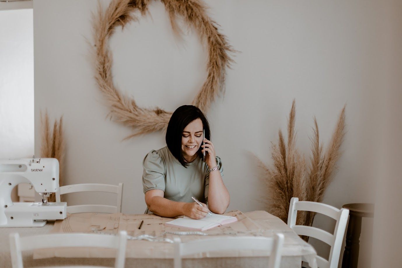 Neutral toned dining room setting with dried pampas grass wreath on beige wall.