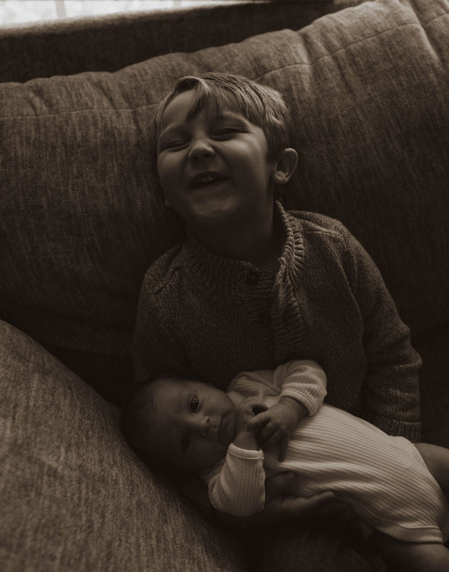 Two siblings sharing a sweet moment while relaxing on a brown couch.