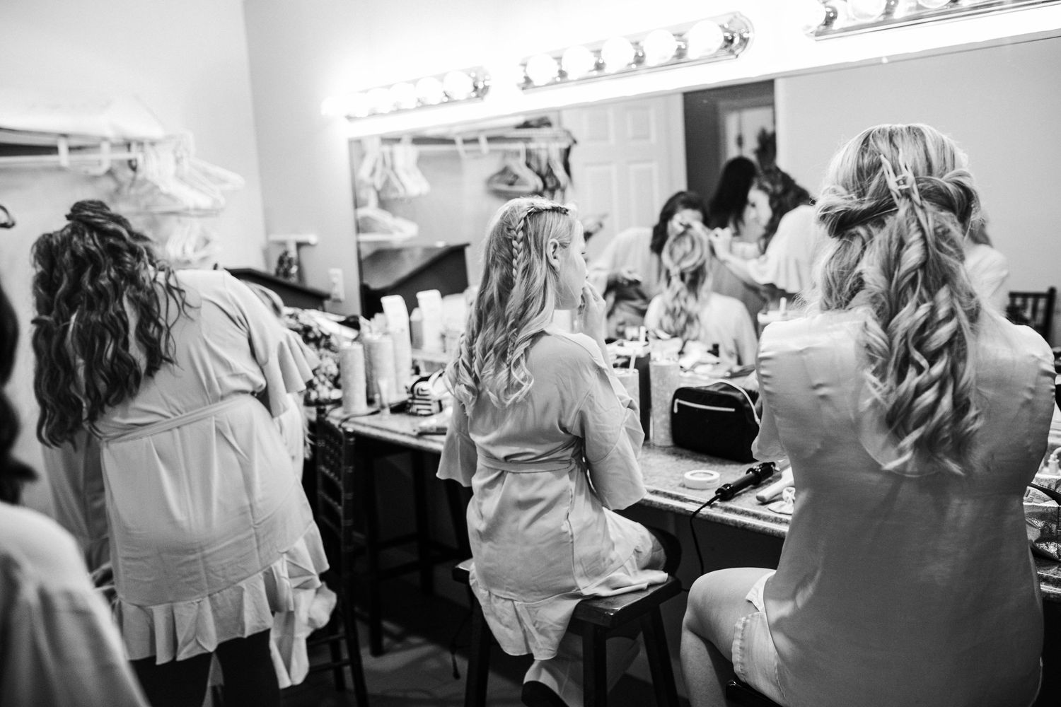 Black and white photo of multiple people sitting at vanity mirrors getting ready backstage in a dressing room.
