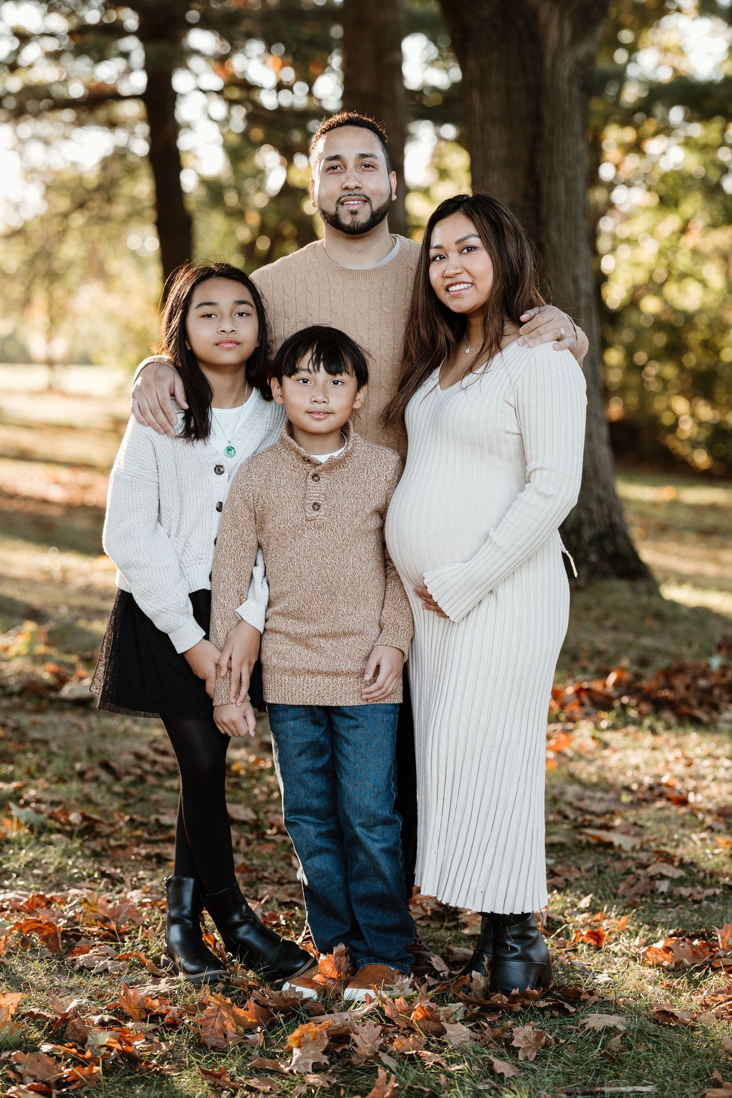 A family of four poses together outdoors in coordinating neutral-colored sweaters during fall.