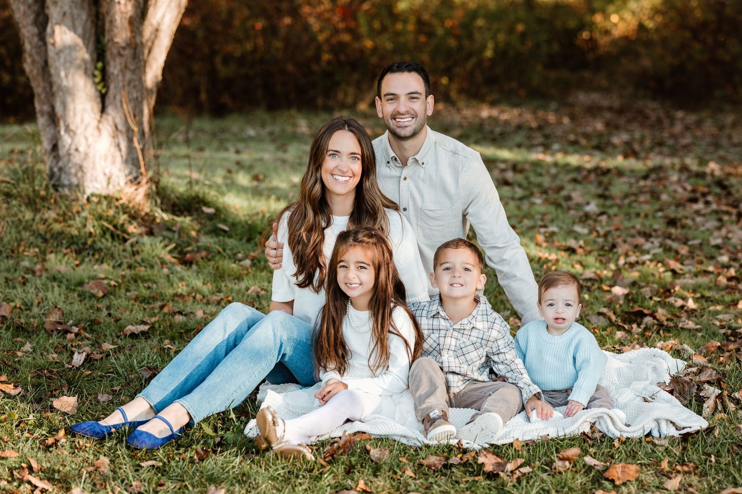 A family of five relaxes on a blanket for an outdoor portrait session in autumn.