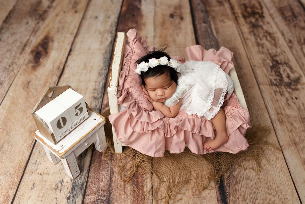 Sleeping newborn in white dress on pink ruffled bedding with vintage radio prop.