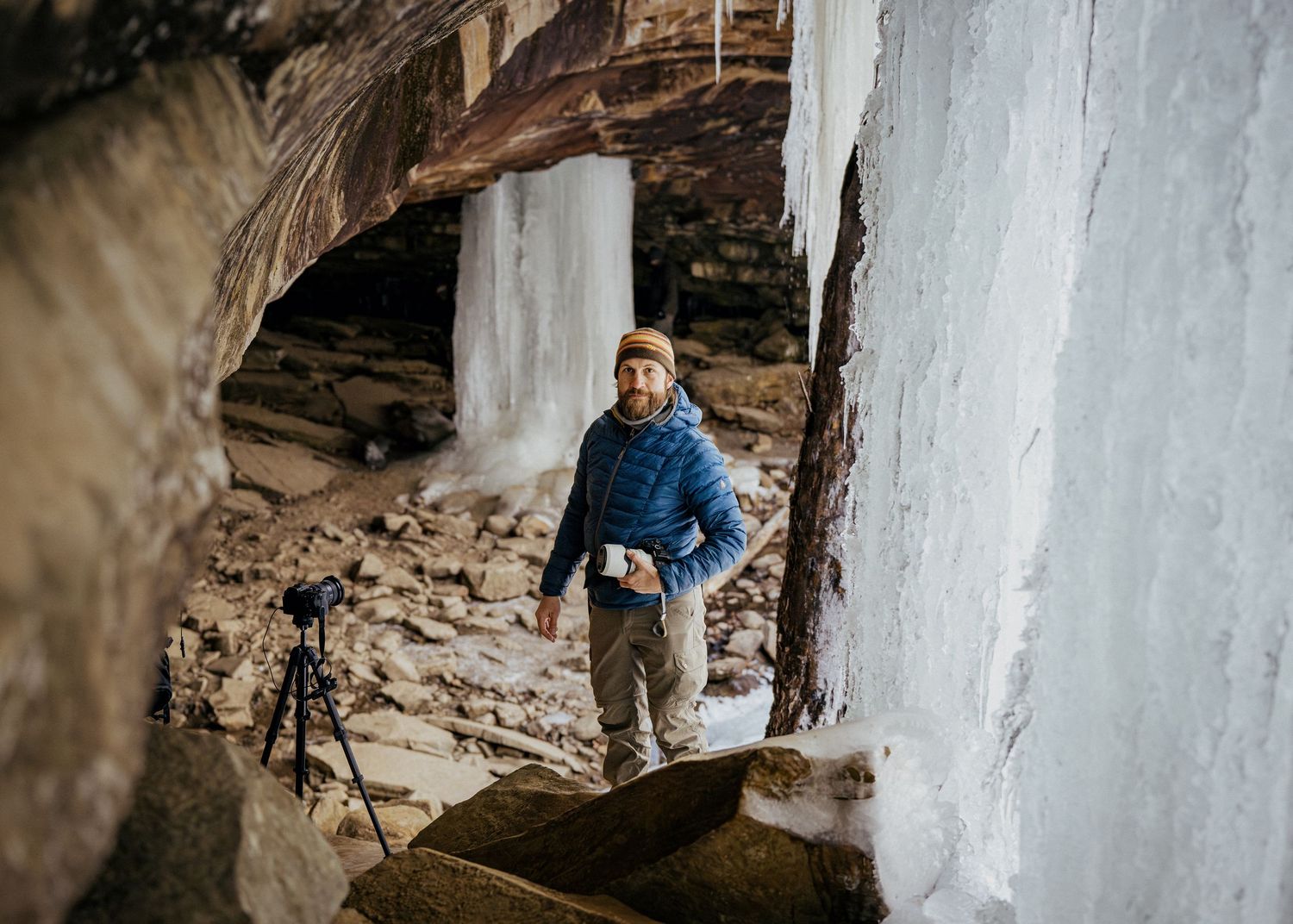 Arkansas nature photographer, Alex Kent poses with camera in hand framed with rock and ice on each side and frozen falls