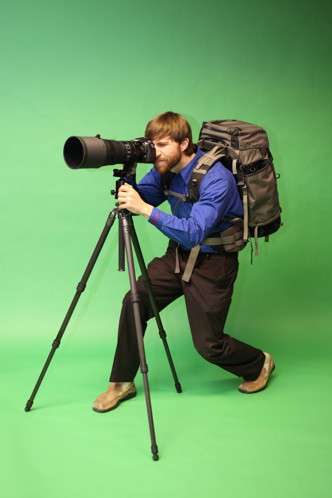 Arkansas commercial photographer, Alex Kent poses on green screen with large super tele lens & camera on tripod.