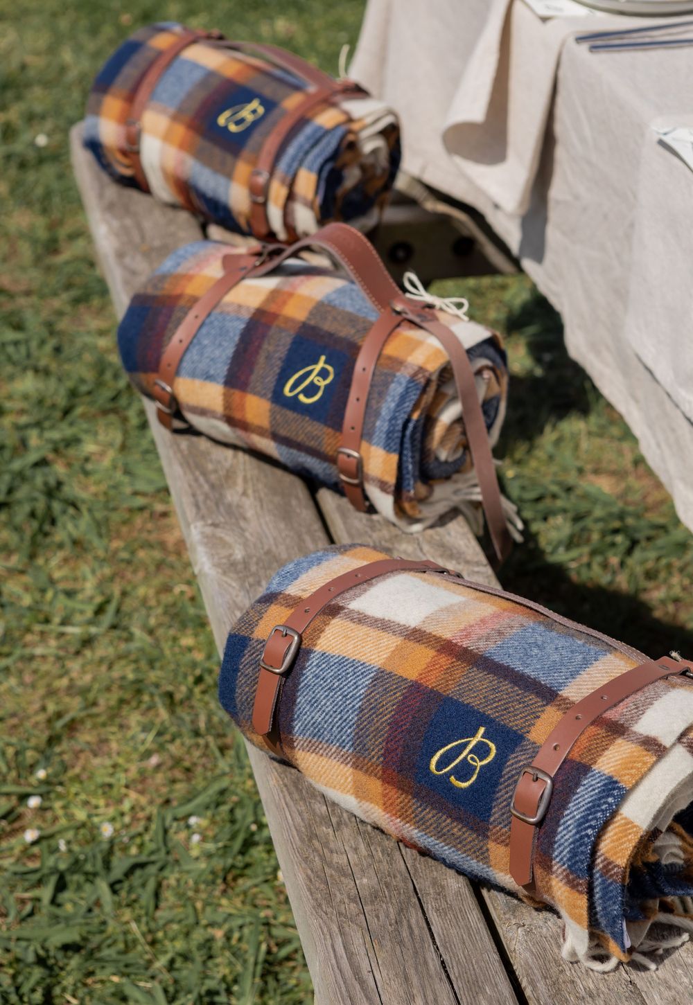 Three plaid wool blanket rolls with leather straps and metallic logos arranged on wooden steps outdoors.