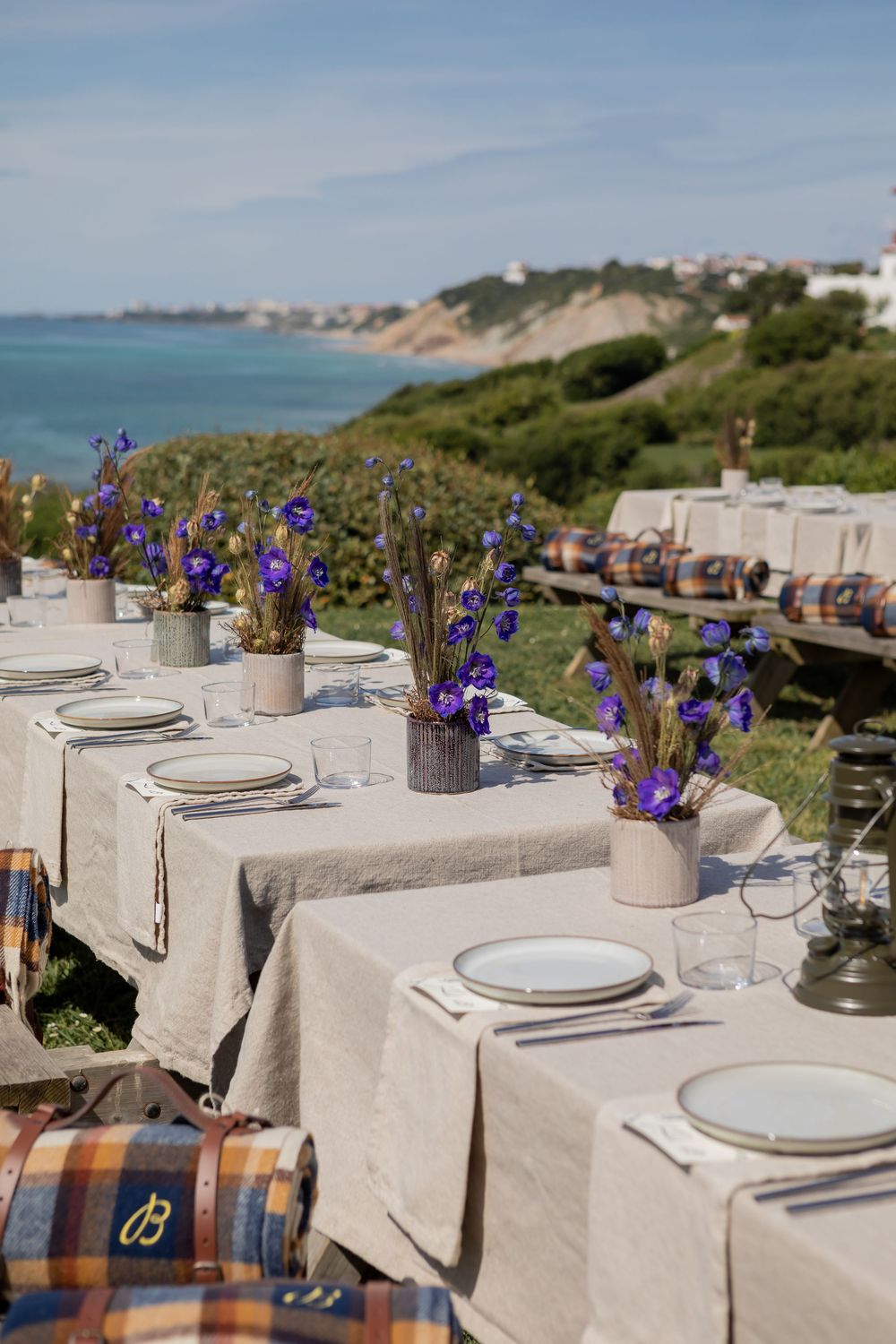 Elegant outdoor dining table setup with white linens, purple iris flowers, and coastal views in the background.