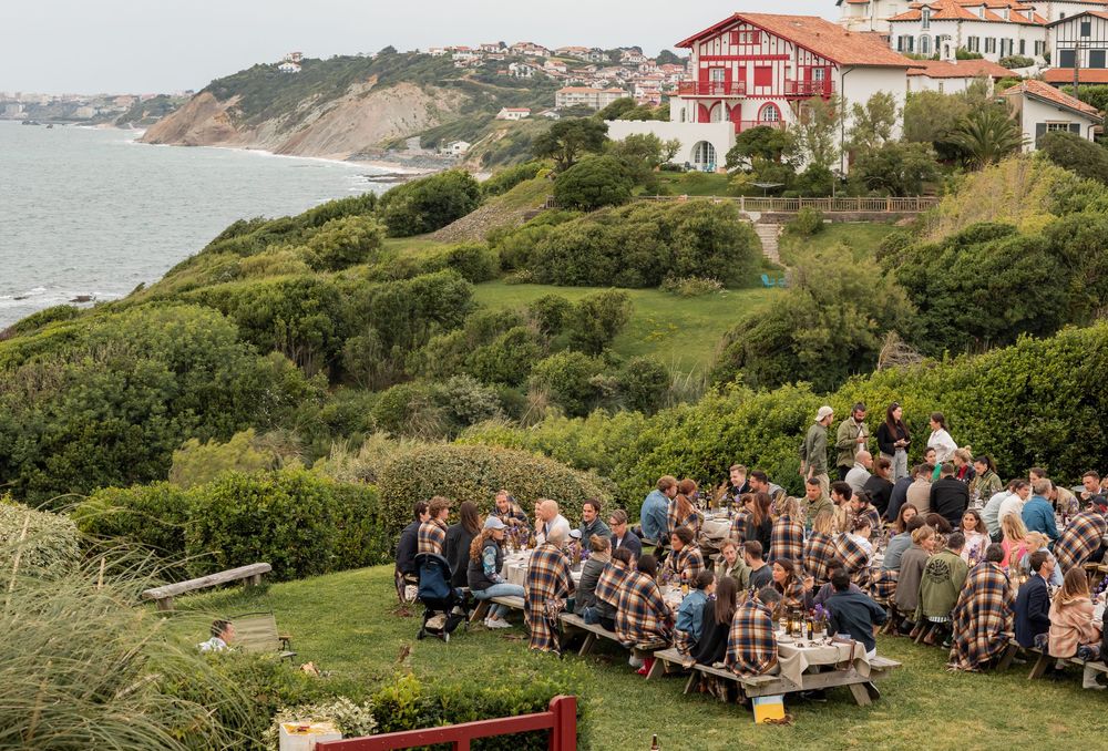 Ocean view wedding ceremony setup with white chairs on lush green cliffside overlooking the sea at sunset.