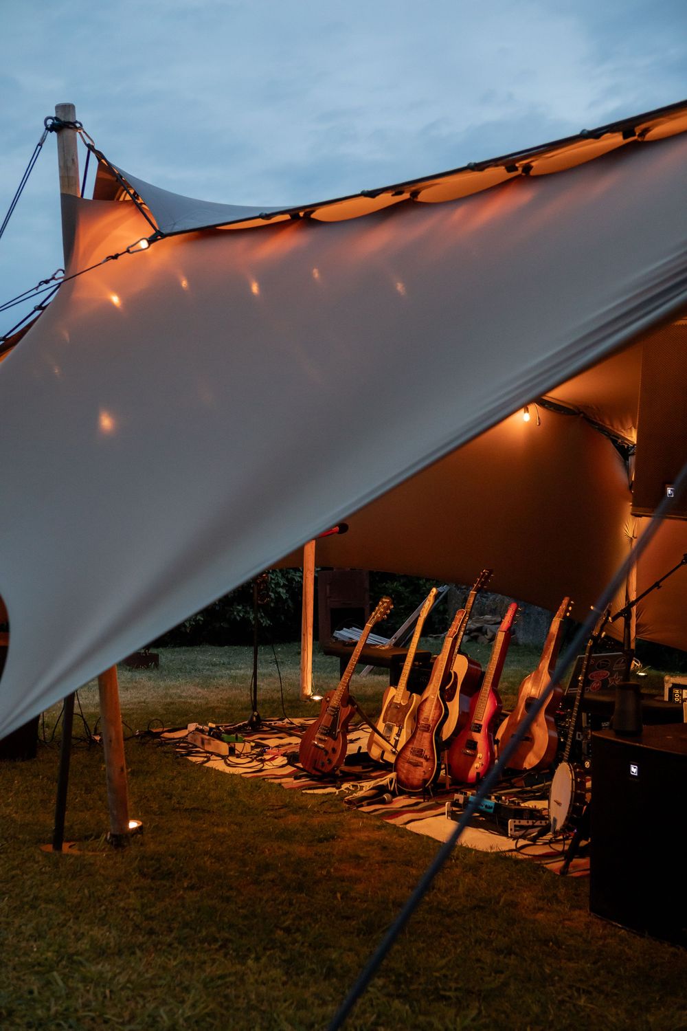 Illuminated stretch tent canopy with lounge chairs set up under warm lighting at sunset creating a cozy outdoor atmosphere.