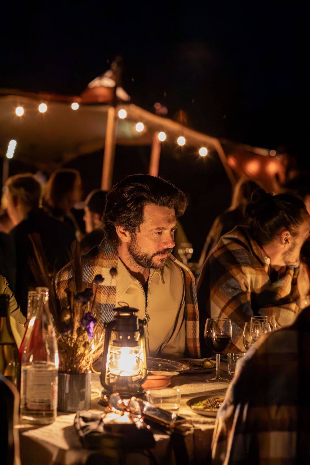 People enjoying an intimate candlelit dinner party with wine glasses and lanterns glowing warmly in the dark.