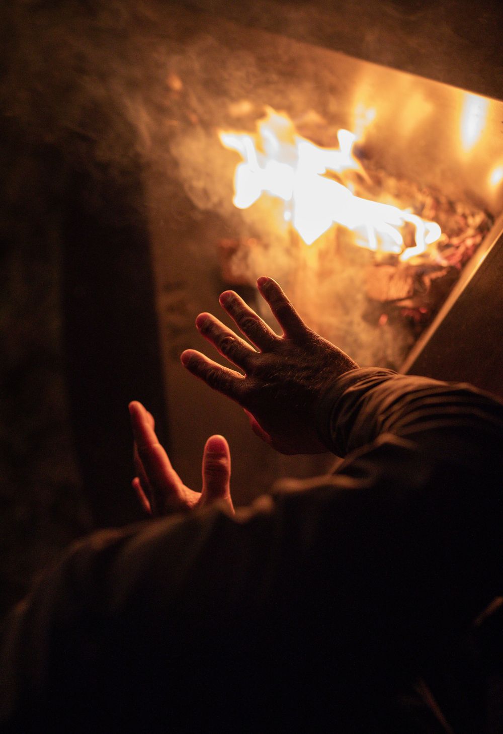 Silhouetted hands reaching toward glowing fire light in darkness create a mystical atmosphere.
